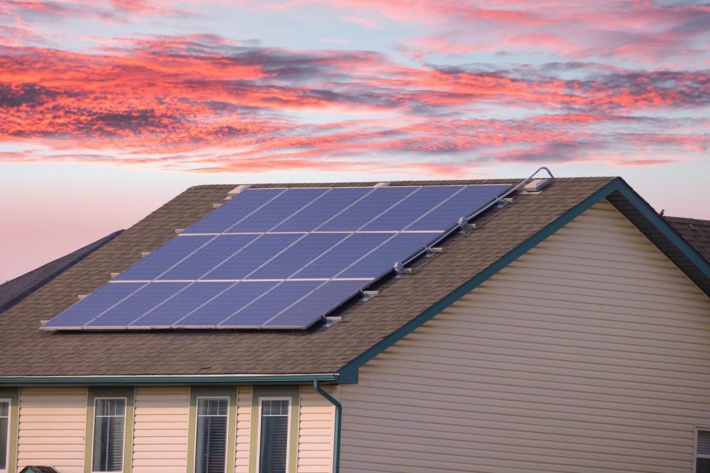 Une maison dont le toit est recouvert de panneaux solaires, coucher de soleil en arrière-plan